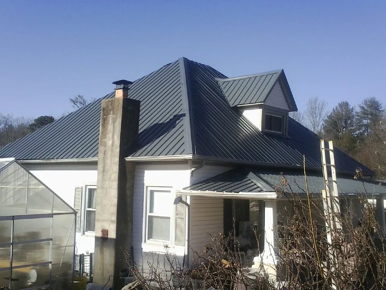 Dark blue standing seam metal roof on a white farmhouse with dormer — Slate & Tile Roof Repair by Roofing Brothers in Morganville