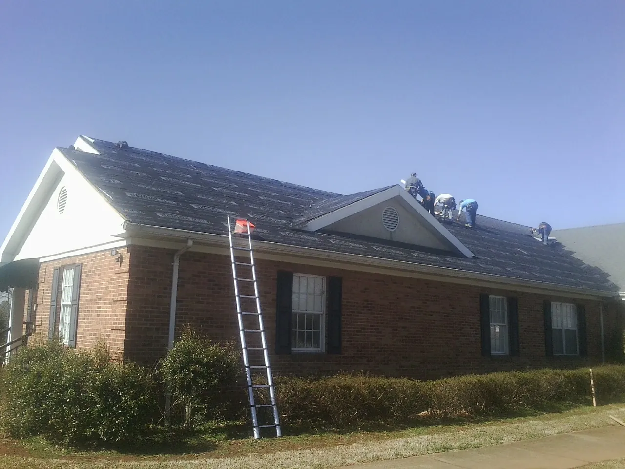 Crew tearing shingles off a brick ranch roof with a ladder set — Emergency Roof Repair work by our crew in Morganville