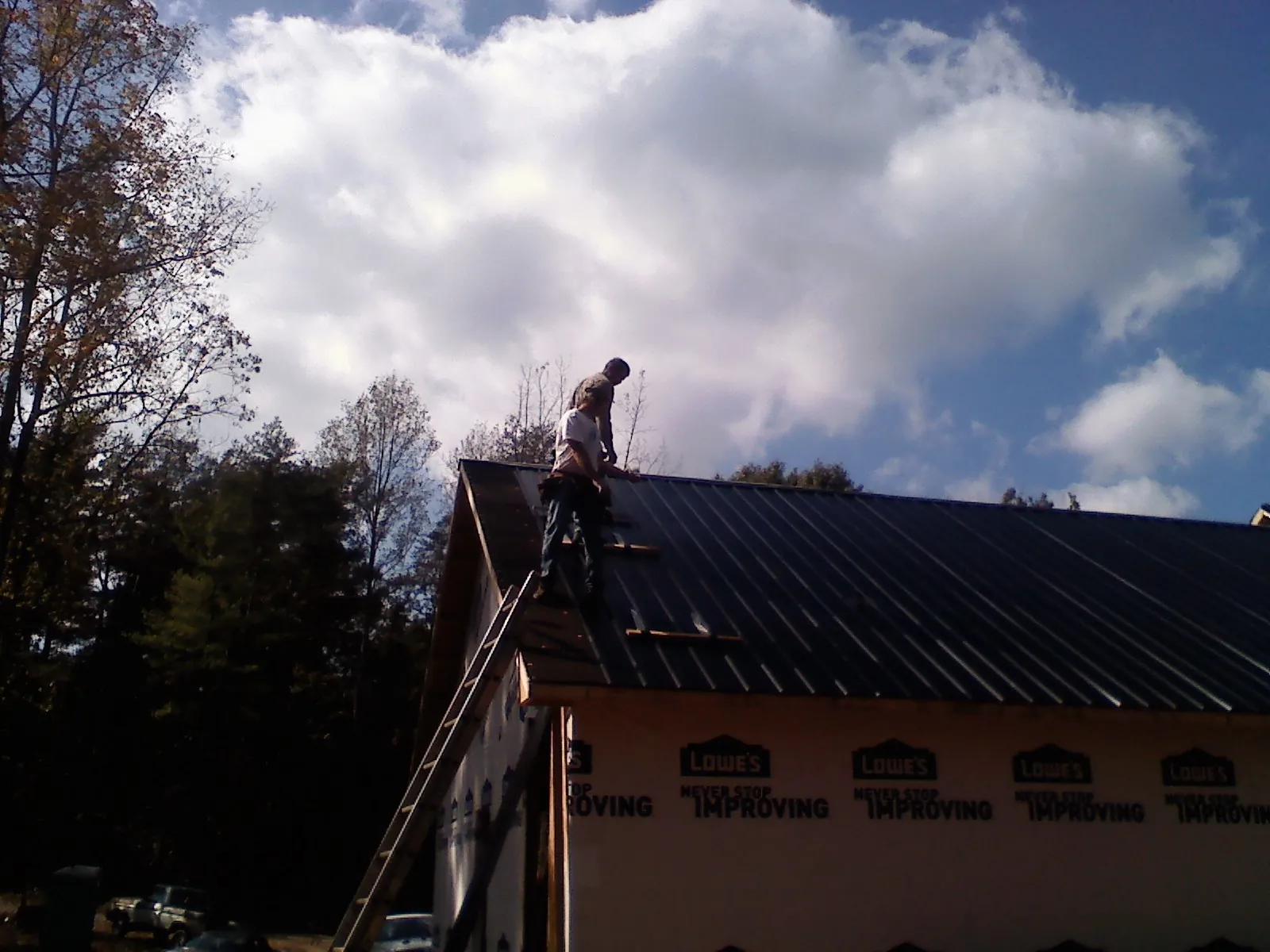 Roofer fastening dark metal panels high against a cloudy sky, from a Roof Inspection job in Morganville