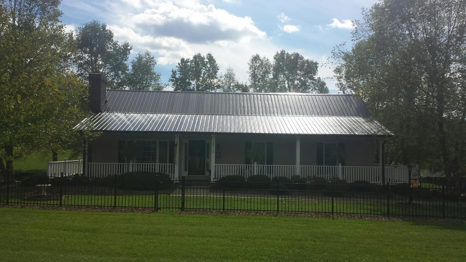 Gray metal roof on a brick ranch with a full width front porch — Gutter Guard Installation work by our crew in Morganville