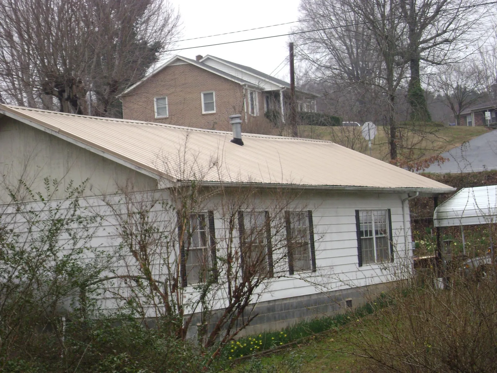Tan metal roof on a white sided house set into a hillside — Commercial Roofing by Roofing Brothers in Morganville