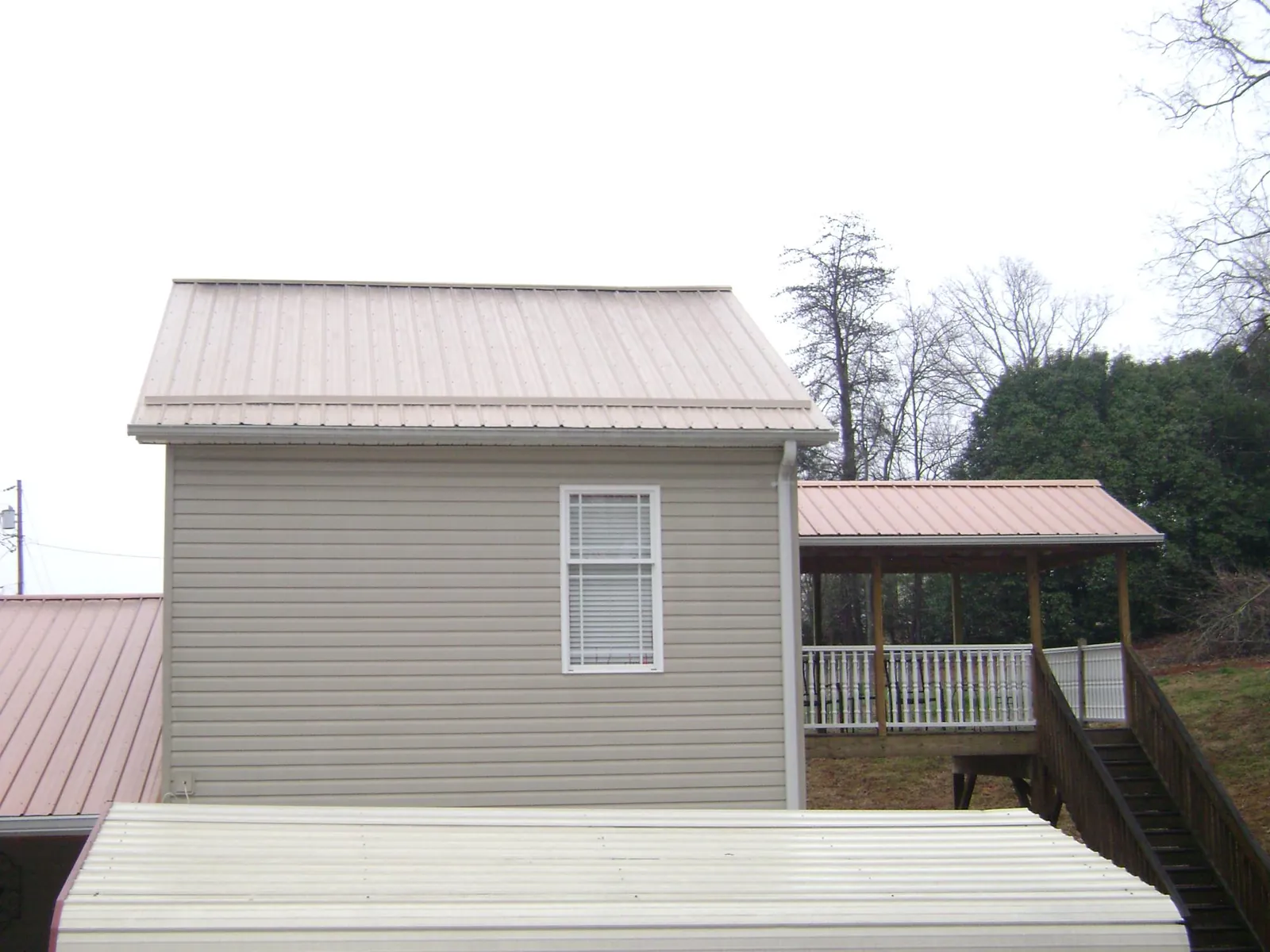 Tan metal roofs on a two story addition and attached porch, from a Roof Replacement job in Morganville