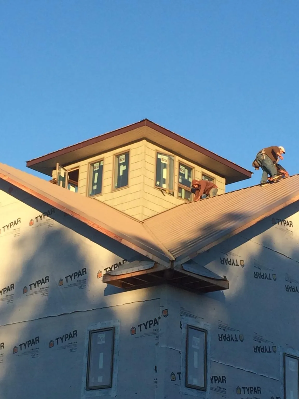 Roofers working around a rooftop cupola on a new metal roof at sunset — Roof Waterproofing in Morganville by Roofing Brothers
